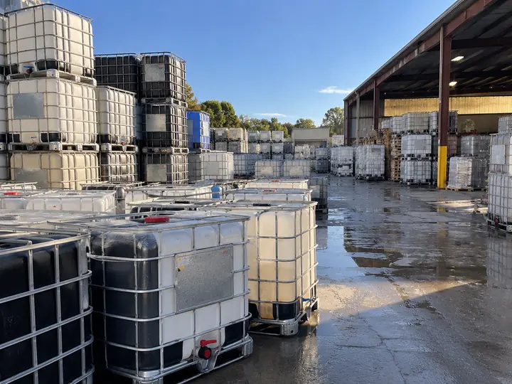 A tote yard after rain with stacks of white and black totes and covered storage under a canopy.